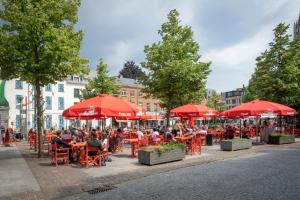 um grupo de pessoas sentadas em mesas sob guarda-chuvas vermelhos em The Black Pants em Antuérpia