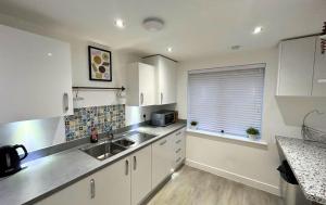 cocina con armarios blancos, fregadero y ventana en High Wycombe Stunning Stylish Four Bedroom House en High Wycombe