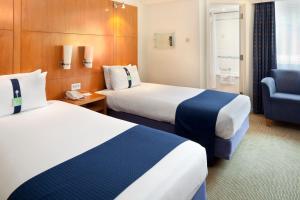 a hotel room with two beds and a chair at Holiday Inn Basingstoke by IHG in Basingstoke