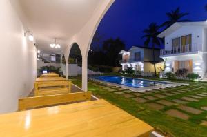 uma fila de bancos de madeira ao lado de uma piscina à noite em Tvessa - A Boutique Hotel em Mandrem