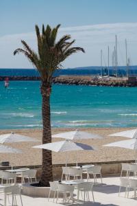 a beach with tables and white chairs and a palm tree at THB El Cid - Adults Only in Can Pastilla