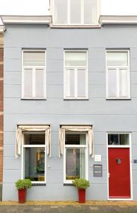 ein graues Haus mit einer roten Tür und Fenstern in der Unterkunft Charming house in city centre Oud-Beijerland in Oud-Beijerland