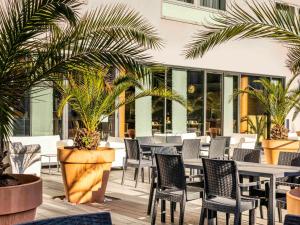 un patio con mesas, sillas y palmeras en Mercure Agen Centre en Agen