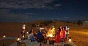 a group of people sitting on the beach at night at Merzouga Luxury Camp in Merzouga