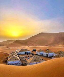 um grupo de tendas no deserto com um pôr-do-sol em Merzouga Luxury Camp em Merzouga