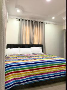 Una cama con una manta de rayas de colores. en Comfortable 2BDR Apt - Superb power supply, Wi-Fi, Kitchen, Netflix, Mins to Airport, en Agege