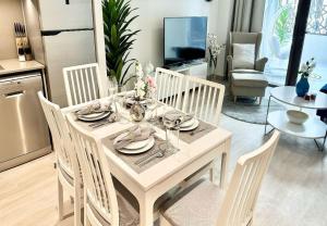 EasyGo - Sunset Creek 1 Bedroom في دبي: طاولة طعام بيضاء مع كراسي بيضاء ومطبخ