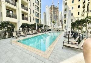a swimming pool with chaises and chairs next to buildings at EasyGo - Sunset Creek 1 Bedroom in Dubai