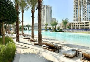 a swimming pool with chaise lounges and palm trees at EasyGo - Sunset Creek 1 Bedroom in Dubai