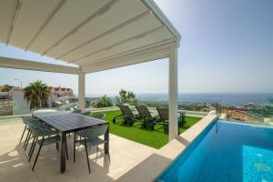 Un patio con mesa y sillas y una piscina. en 200m NEW Villa E with priv/heated pool, ocean view., en Adeje