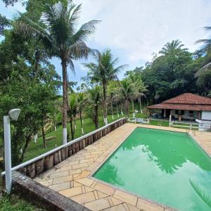 a swimming pool in front of a house with palm trees at Rancho Leguian in Cachoeiras de Macacu