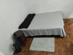 a white bed with a black pillow and a rug at Aphostel gatinhos perça caiçara in Santos