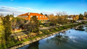 a building with an orange roof next to a river at Regia Panzió in Halászi