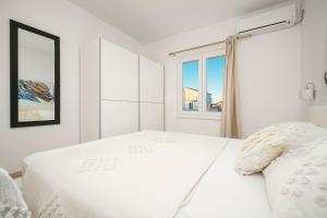 a white bedroom with a large bed and a window at Apartments Tomić in Vodice