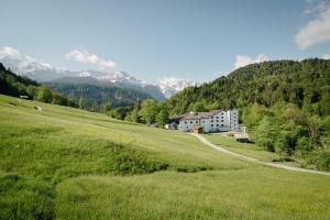 una casa in un campo verde con montagne sullo sfondo di Das Graseck - mountain hideaway & health care a Garmisch-Partenkirchen