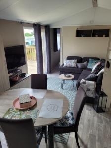 een woonkamer met een tafel en een bank bij Mobilhome tout confort, proche Saint-Malo, à 50 m de la plage et du GR34 in Saint-Coulomb