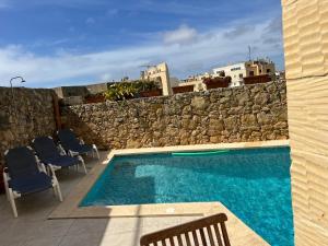 a swimming pool with chairs and a stone wall at 4 Bedroom Holiday Home with Private Pool & Views in Xewkija