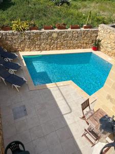 une piscine avec des chaises et un mur en pierre dans l'établissement 4 Bedroom Holiday Home with Private Pool & Views, à Xewkija