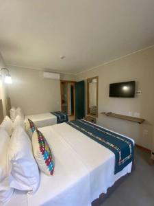 ein Hotelzimmer mit einem großen weißen Bett mit Kissen in der Unterkunft Eco Resort Quinta Santa Bárbara Ap 101/11 bloco E in Pirenópolis