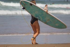 una mujer caminando por la playa sosteniendo una tabla de surf en Welle Surf Morocco, en Taghazout