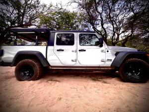 a white jeep parked in the sand with its doors open at Embark on a journey through Maui with Aloha Glamp's jeep and rooftop tent allows you to discover diverse campgrounds, unveiling the island's beauty from unique perspectives each day in Paia