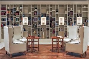 a library with three chairs and two tables and bookshelves at H10 Suites Lanzarote Gardens in Costa Teguise