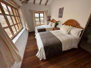 a bedroom with two beds and two windows at Parwa Guest House in Ollantaytambo