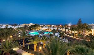 a resort with a pool and palm trees at night at H10 Suites Lanzarote Gardens in Costa Teguise
