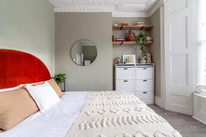 1 dormitorio con 1 cama con cabecero rojo y espejo en Arte Stays - 2 Bed Luxurious Flat, Garden, 5min Dalston st., Parking Available, Serviced Accommodation - up to 5 ppl en Londres