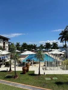 un complexe avec une piscine bordée de palmiers et de parasols dans l'établissement Refúgio Beira Lago- Life Resort, à Brasilia