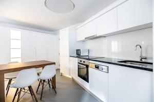 a white kitchen with a wooden table and white chairs at Historic Town Cascais Modern Apartment in Cascais