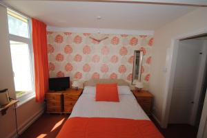 a bedroom with a bed with orange sheets and a television at The Curraghmore in Shanklin