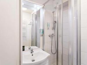 La salle de bains blanche est pourvue d'un lavabo et d'une douche. dans l'établissement Aparthotel Adagio Access Paris Saint-Denis Pleyel, à Saint-Denis