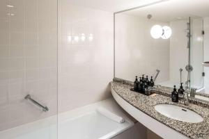 a white bathroom with a sink and a shower at The Atrium Hotel & Conference Centre Paris CDG Airport, by Penta in Roissy-en-France