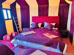 a bedroom with a large bed with purple sheets and pillows at Arena Desert Camp & Activitys in Merzouga