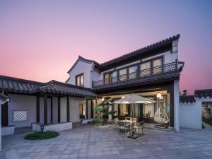 ein Haus mit einer Terrasse mit Tischen und einem Sonnenschirm in der Unterkunft Yangzhou Mangdao Garden Resort in Yangzhou