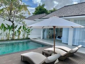 an umbrella and chairs next to a swimming pool at Alami Luxury Villa in Seminyak