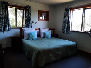 a bedroom with a bed with blue sheets and windows at Eden's Edge Lodge in Motueka