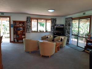 una sala de estar con sillas y mesa y una habitación con ventanas en Eden's Edge Lodge, en Motueka