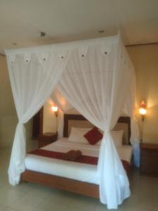 a bedroom with a bed with white curtains at Pondok Aldi in Amed