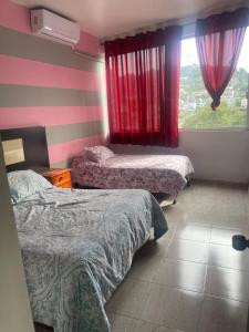 a room with two beds and a window with red curtains at Departamentos grandes y centricos. in Poza Rica de Hidalgo