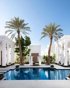 einem Pool mit Palmen vor einem Gebäude in der Unterkunft Raffles Al Areen Palace Bahrain in Manama