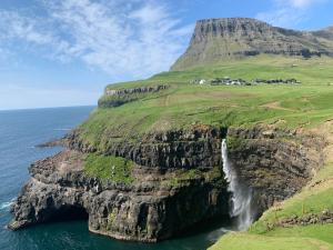 a waterfall on a cliff next to the ocean at Peter’s guesthouse in Sandavágur