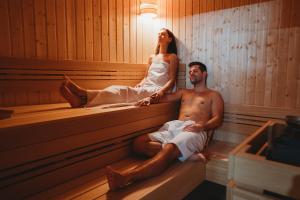 a man and woman sitting in a sauna at Spa & Wellness Hotel Fitak**** in Liptovský Ján