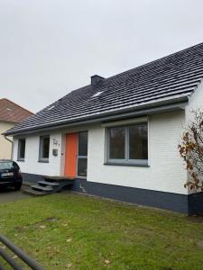 Biały i pomarańczowy dom z samochodem przed nim w obiekcie Rogge, Ferienhaus w mieście Fintel