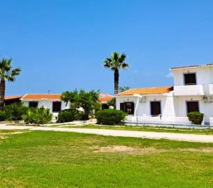 a white house with palm trees in a yard at Kefalonia Beach Hotel & Bungalows in Lixouri