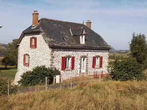 uma antiga casa de pedra com janelas vermelhas numa colina em Grande maison 7 chambres em Cheylade