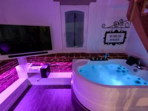 een badkamer met een bad, een tv en paarse verlichting bij L'Antre vue - jacuzzi au château in Belberaud