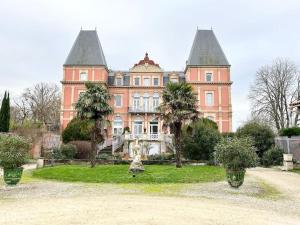 L'Antre vue - jacuzzi au château في Belberaud: مبنى وردي كبير أمامه أشجار نخيل
