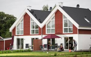 a red and white house with people sitting under an umbrella at Ferienhaus Nordhorn - Haus Am See in Nordhorn